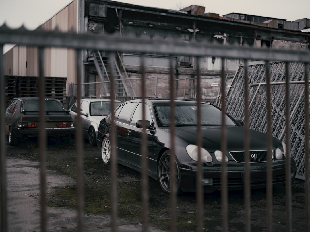 Two cars parked in a parking lot behind a fence