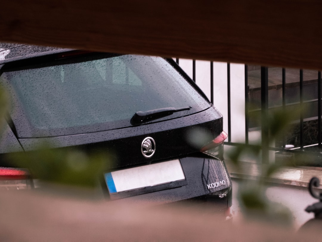 A black car is parked behind a fence.