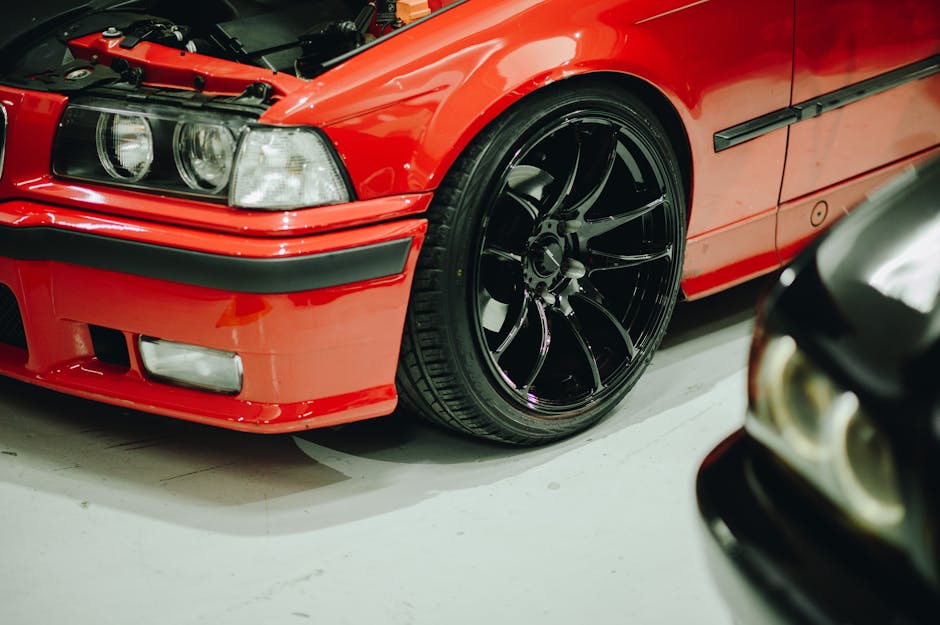 Detailed view of a red BMW E36 with custom rims in a garage setting.
