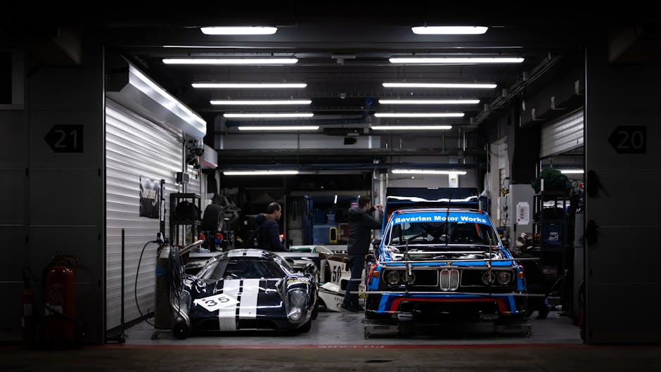 Classic BMW and race cars in a garage at night, showcasing automotive passion.