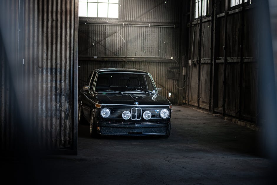 A sleek vintage BMW is parked inside a dimly lit industrial garage, exuding timeless elegance.