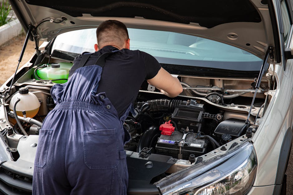 Mechanic in overalls working on a car engine outdoors, showcasing vehicle repair skills.