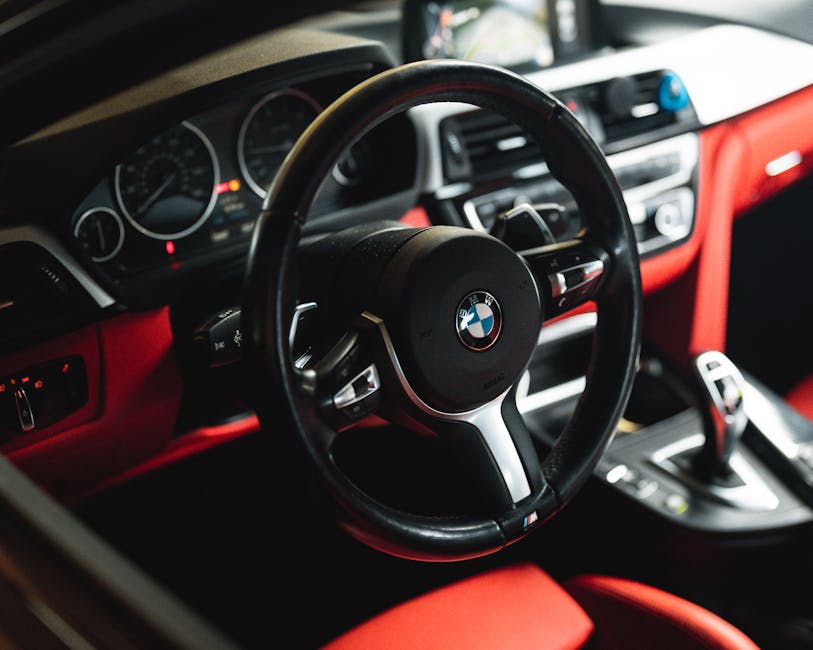 Close-up view of BMW car interior showcasing the steering wheel and dashboard with luxurious red accents.